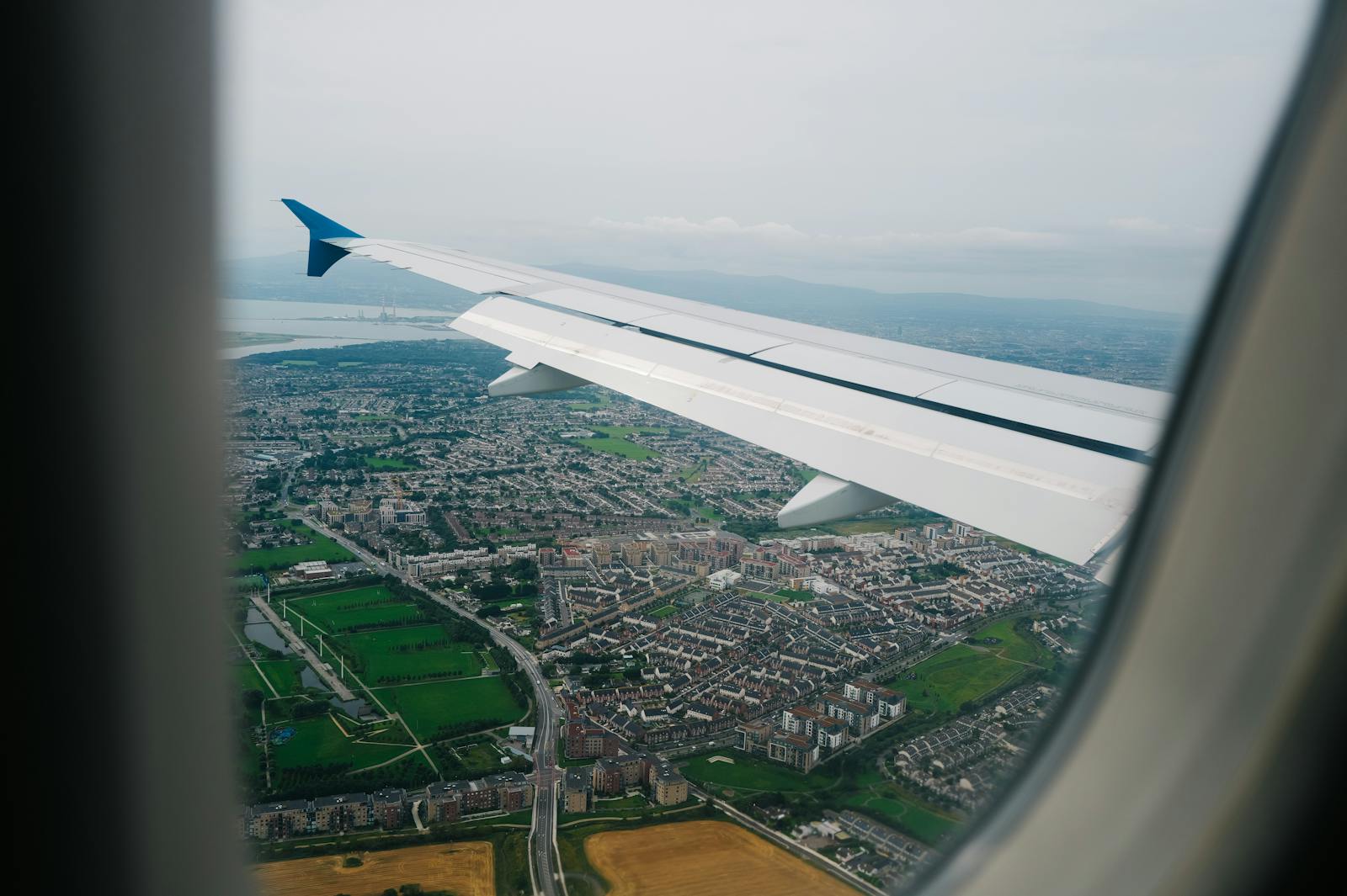 Photo by Adrien Olichon View from an airplane window showing a vibrant cityscape and landscape below, highlighting the journey.